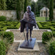 Monumental Traditional Elder Walking Figure Bronze Statue by Giant Sculptures, 230cm dark patinated figure with staff and shawl, displayed in a formal hedged garden.