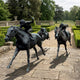 Monumental Traditional Galloping Racehorses and Jockeys Bronze Sculpture by Giant Sculptures, dark patina horses mid-gallop with lead jockey raising whip, on stone terrace.