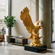 Monumental Traditional Golden Eagle Bronze Sculpture by Giant Sculptures, wings raised and beak open on a black plinth in a stone-clad lobby beside a fiddle-leaf fig.