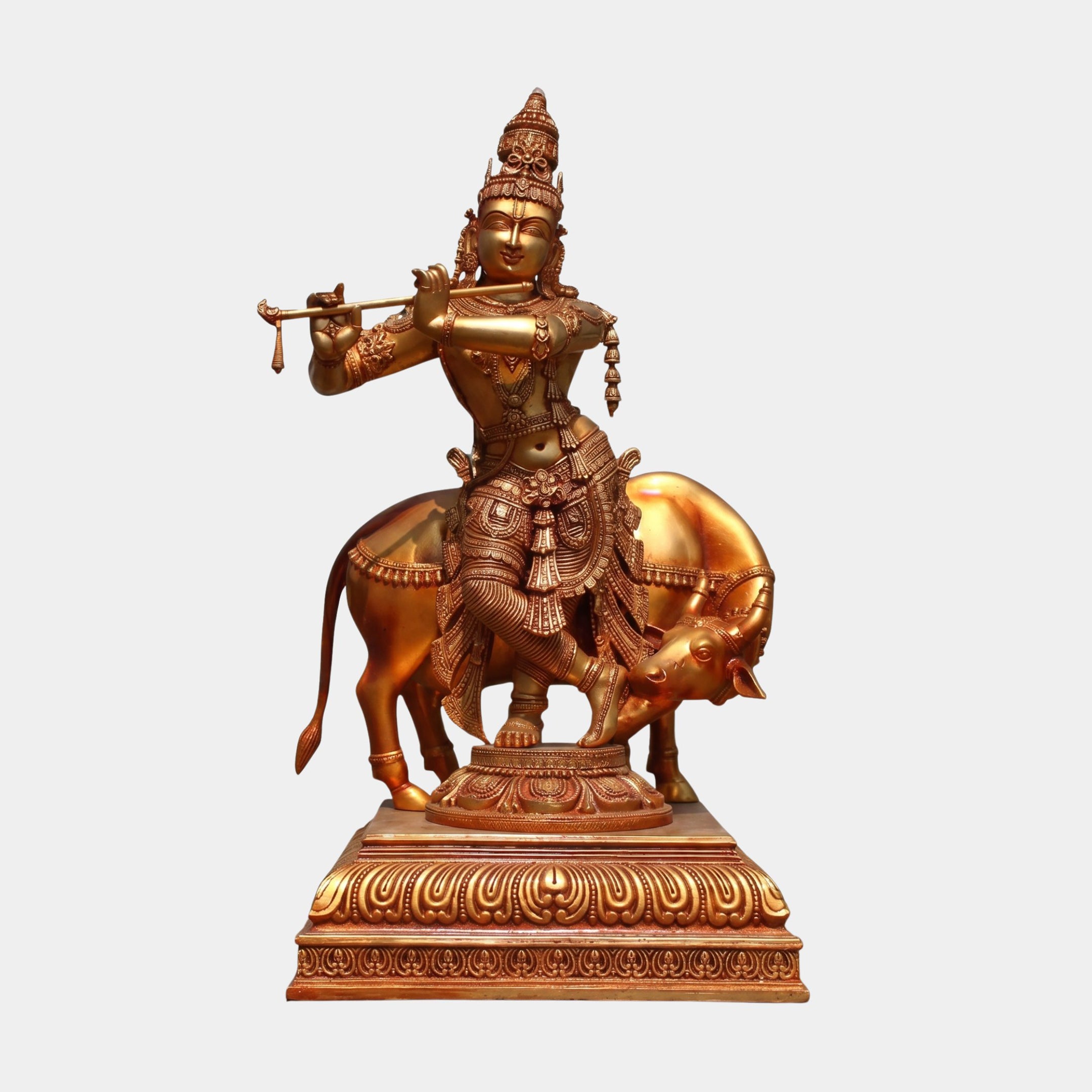 Monumental Traditional Krishna and Sacred Cow Bronze Sculpture by Giant Sculptures, polished golden-bronze figure playing flute beside a bowed cow on a tiered plinth.
