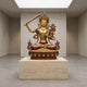 Monumental Traditional Manjushri Seated Bronze Sculpture by Giant Sculptures, gilded with reddish-brown robes, on a travertine plinth in a skylit gallery.