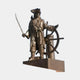 Monumental Traditional Pirate Captain Bronze Sculpture by Giant Sculptures, cutlass raised and hand on ship's wheel, golden-brown patina, plain background.