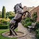 Giant Sculptures Monumental Traditional Rearing Horse Bronze Sculpture with dark brown patina, displayed on a gravel circle in a walled garden beside a bench.