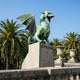 Monumental Traditional Rearing Winged Dragon Bronze Sculpture by Giant Sculptures with verdigris patina, mid-roar on a stone plinth among palm trees.