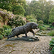 Monumental Traditional Roaring Tiger Bronze Sculpture by Giant Sculptures, mid-lunge with dark patina and verdigris base, on a stone garden patio beside a lily pond.