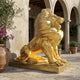 Giant Sculptures Monumental Traditional Seated Roaring Lion Bronze Sculpture in polished gold finish, shown in a Mediterranean courtyard with stone arches and olive trees.
