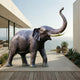 Monumental Traditional Standing Elephant Bronze Sculpture by Giant Sculptures with raised trunk and pale gold tusks on a modern oceanview terrace.