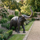 Monumental Traditional Standing Elephant Bronze Sculpture by Giant Sculptures with raised trunk and gold tusks, set on a walled garden path beside roses and lavender.