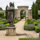 Monumental Traditional Standing Male Figure Bronze Statue by Giant Sculptures, 400cm, in kurta and turban with folded arms, on a stone plinth in a formal garden.