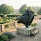 Monumental Wild Boar Head Bronze Sculpture by Giant Sculptures on a stone plinth overlooking a formal garden and tree-lined avenue to a distant manor house.