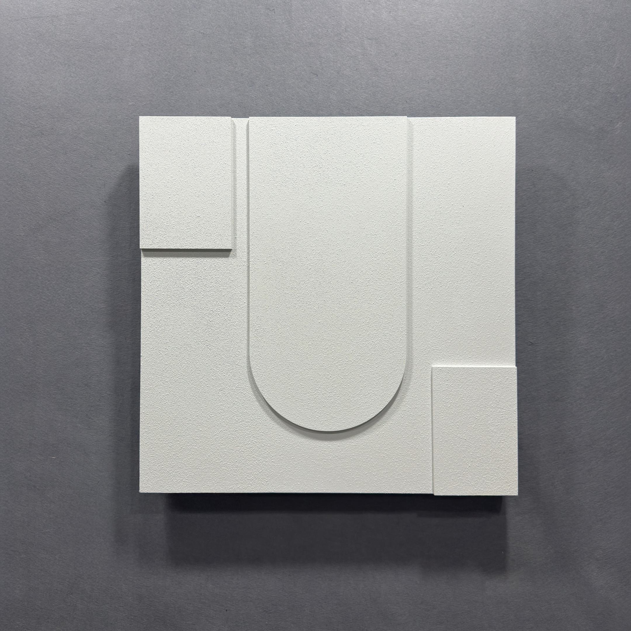 The Moro III Triptych White Relief 3D Wall Art by Giant Sculptures showcases raised geometric shapes, including a central U shape and corner rectangles on a gray background, for a stunning minimalist sandstone effect.