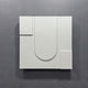 The Moro III Triptych White Relief 3D Wall Art by Giant Sculptures showcases raised geometric shapes, including a central U shape and corner rectangles on a gray background, for a stunning minimalist sandstone effect.