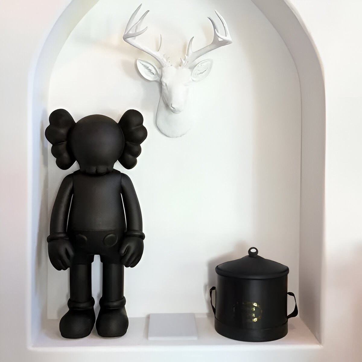 The Giant Sculptures Midnight Black Iconify Standing Figure - 20cm is placed beside a sleek black metal container with handles. A white deer head sculpture above completes the striking contemporary interior décor display.