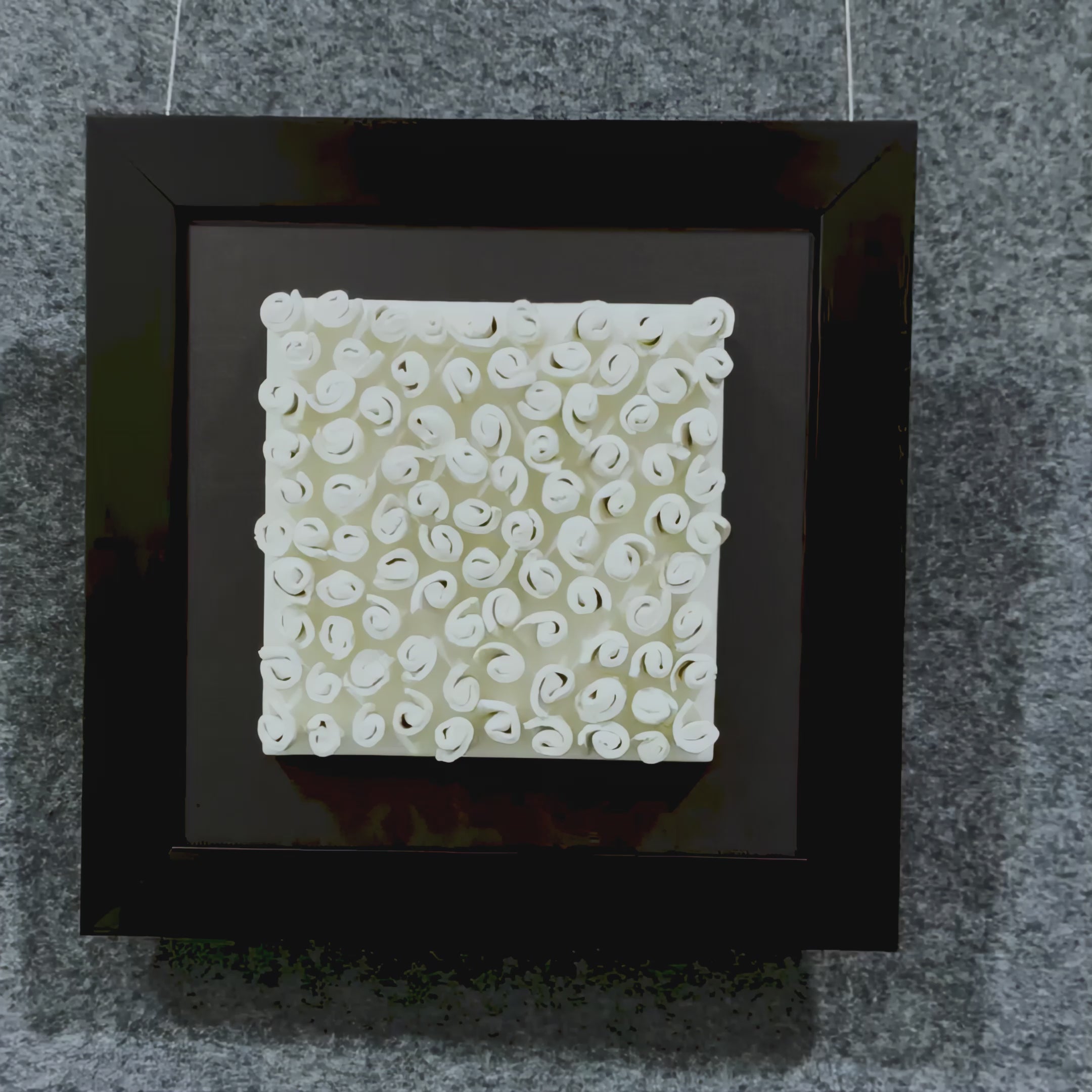 Cream ceramic spirals twist in neat formation, creating rich texture and rhythm against a dark textile base and minimal black frame