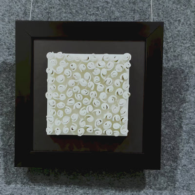 Cream ceramic spirals twist in neat formation, creating rich texture and rhythm against a dark textile base and minimal black frame