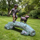 Traditional Boy and Dog Bronze Sculpture by Giant Sculptures, 150cm, showing a child crossing a verdigris log with a small dog, displayed on a lawn.