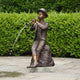 Traditional Boy Playing Flute Fountain Bronze Sculpture by Giant Sculptures, seated on a rock with water arcing from the flute, set on a garden patio.