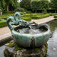 Traditional Chinese Dragon Bronze Fountain by Giant Sculptures, with two verdigris dragons coiled across a hemispherical basin spouting water, set on mossy stone in a formal hedged garden.