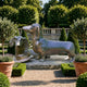 Traditional Dachshund Pair Bronze Sculpture by Giant Sculptures displayed on a stone plinth in a formal garden with topiary, lavender, and terracotta pots.