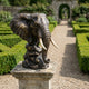 Traditional Elephant Head Bronze Bust by Giant Sculptures on a stone plinth in a formal hedged garden, with ivory-toned tusks and dark patina.