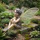 Traditional Fairy Boy Child Bronze Sculpture by Giant Sculptures, seated on a mossy stone in a lush garden with iridescent gold-veined wings extended.