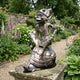 Traditional Laughing Goblin on Tortoise Bronze Sculpture by Giant Sculptures, warm brown patina, displayed on a stone plinth in a flower-filled garden path.