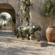 Traditional Prowling Panther Bronze Sculpture by Giant Sculptures with verdigris patina on a marble base, displayed on a stone courtyard near wisteria.