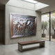 Traditional Three Elephants Advancing Bronze Relief by Giant Sculptures mounted on a concrete wall above a wooden bench in a skylit minimalist interior.